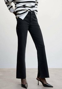 Pantalones de mezclilla negros de campana con dobladillo deshilachado, con un ajuste de altura media. Combinados con un suéter a rayas blanco y negro y tacones negros puntiagudos.