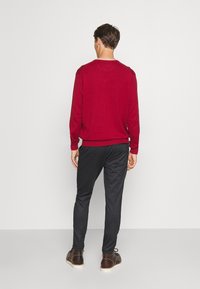 Pull marron, poignets côtelés, coupe décontractée ; pantalon gris foncé avec des jambes fuselées ; chaussures marron avec une semelle claire. Fond blanc uni.