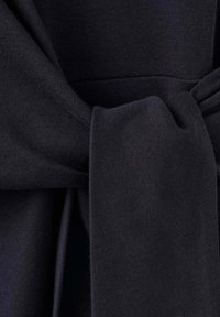 Gros plan d'une ceinture en tissu noir nouée sur un vêtement assorti, montrant la texture tissée et le détail du nœud.