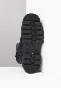 Black boot with a textured upper, side zip closure, and a robust rubber sole featuring deep tread patterns for traction. Marked with brand logo.