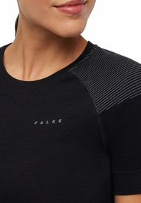 Czarna koszulka z okrągłym dekoltem, z poziomymi paskami na ramieniu. Nazwa marki "FALKE" nadrukowana jest na przodzie na biało.