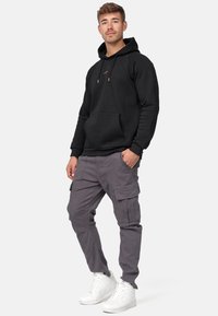 Sudadera negra con bolsillo frontal, combinada con pantalones cargo grises que cuentan con múltiples bolsillos y zapatillas altas blancas.