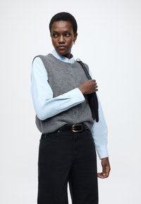 Szary wełniany kamizelka na jasnoniebieskiej koszuli zapinanej na guziki, w połączeniu z czarnymi dżinsami. Strój uzupełnia pasek z złotą klamrą i czarnym paskiem.