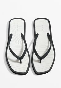 Zwarte rubberen flip-flops met een gevoelige witte binnenzool voorzien van gebogen lijnen, dunne banden en een centrale teenzool.