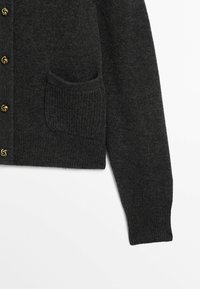 Cardigan gris charbon en tissu tricoté doux, avec une texture côtelée, une poche passepoilée et des fermetures à boutons dorés.