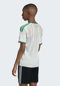 Maillot de sport blanc avec accents verts et rouges, présentant des épaules rayées et des détails perforés. Short noir avec trois bandes.