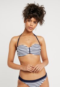 Stripet bikini sett i marineblått og hvitt, med et bandeau-top med en midtklips og matchende truser. Glatt stoff, halterstropper.