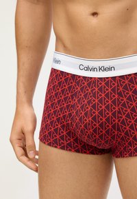 Czerwone i granatowe bokserki z geometrycznym wzorem, z białą elastyczną taśmą z logo marki Calvin Klein oraz gładkim bawełnianym materiałem.
