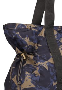 Torebka tote w kolorze granatowym i beżowym w kwiatowy wzór, wykonana z wytrzymałego materiału. Posiada zapięcie na sznurek i mocne czarne ramiączka.