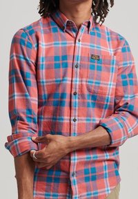 Red and blue plaid long-sleeve shirt made of flannel fabric, featuring a button-down collar, chest pocket, and rolled sleeve detail.