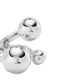 Escultura de metal plateado con superficies suaves y reflectantes y varias formas esféricas conectadas por un brazo curvado.