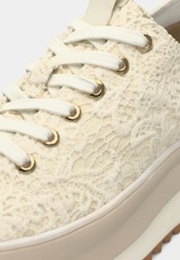 Δετά παπούτσια σε λευκό ύφασμα με υφή και σχέδιο δαντέλας, χρυσές οπές κορδονιών και κρεμ καουτσούκ σόλα με καφέ τάπα.