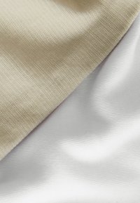 Kaksi päällekkäin olevaa kangasnäytettä: yksi beige, jossa on teksturoitu, poimuinen pinta, ja toinen sileä, valkoinen kangas, molemmissa pehmeitä poimuja.
