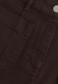 Tessuto denim marrone scuro con una tasca frontale e dettagli di cucitura visibili. Texture liscia con una leggera lucentezza. Accento con bottone in metallo.