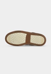 Semelle de chaussure avec bord marron et bande de roulement beige présentant des motifs circulaires et tissés sur un fond blanc uni.