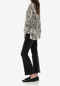 Bluzka w czarno-białe paski zebry, wykonana z lekkiego materiału, w połączeniu z czarnymi dżinsami w kant i czarnymi loafersami. Widok z profilu.