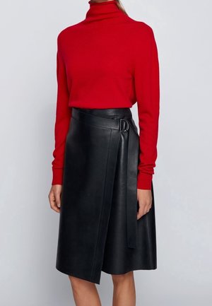 Suéter de cuello alto rojo combinado con una falda corta de cuero negro con cierre lateral y textura suave, que llega hasta la mitad de la pantorrilla.