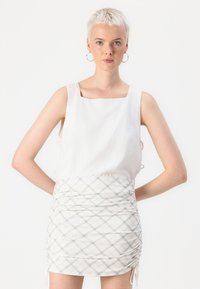 White sleeveless top with a square neckline, paired with a ruched plaid mini skirt featuring gray and beige tones and side ties.