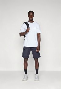 Biała koszulka z krótkim rękawem i kieszenią na piersi, granatowe szorty cargo z bocznymi kieszeniami, do tego białe tenisówki i czarne skarpetki.