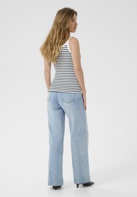 Top sans manches à rayures noir et blanc associé à un jean large bleu clair, tous deux présentant une coupe décontractée et des détails minimes.