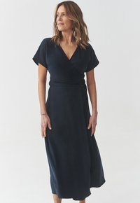 Abito avvolgente blu navy realizzato in tessuto morbido, con maniche corte, scollatura a V profonda e chiusura con bottone laterale, che arriva fino a metà polpaccio.