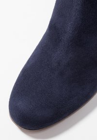Stivale alla caviglia in suede blu navy con superficie liscia, punta rotonda e silhouette classica, caratterizzato da una leggera lucentezza e design minimalista.