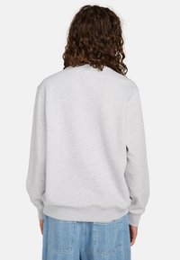 Sudadera gris con cuello redondo clásico y puños acanalados, que presenta una textura suave. Combinada con jeans azules de estampado.