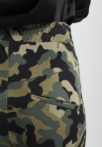 Kamouflage-mönstrade byxor i grön och svart, med resåren i midjan och en bakficka med en ren finish. Mjukt, stretchigt tyg.