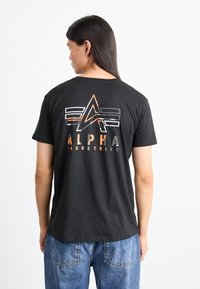Tricou negru din bumbac, cu un design grafic multicolor, având cuvântul "ALPHA" scris cu litere îngroșate, forme geometrice și o croială lejeră.