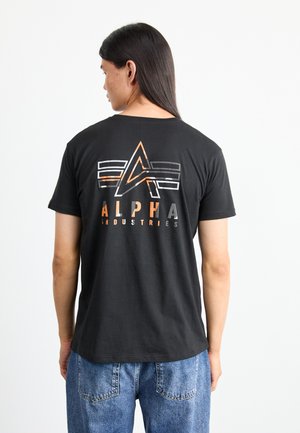 T-shirt in cotone nero con un design grafico multicolore che presenta "ALPHA" in caratteri grassetto, forme geometriche e una vestibilità rilassata.