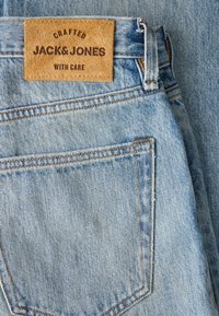 Светлосини дънки от деним с кафява кожена лепенка, на която е написано "Crafted Jack & Jones With Care", разположена над задния джоб.