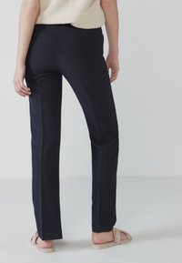 Navyblauwe op maat gemaakte broek met een rechte pijp, voorzien van twee achterzakken en een gladde, matte textuur. Gemaakt in combinatie met beige sandalen.