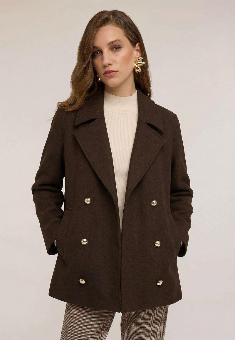 Ruskea villainen merimiespuku kaksirivisellä napituksella, hopeanvärisillä napeilla, leveillä kauluksilla ja sivutaskuilla. Vuorattu teksturoidulla, vaalealla kankaalla.