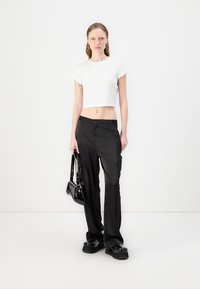White cropped t-shirt, black cargo pants with pockets, chunky black platform shoes, and a small black handbag. Simple design and minimal details.