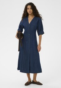 Jeans obleka z globokim V-izrezom in kratkimi napihnjenimi rokavi, z sprednjimi gumbi, dolgim krilom do tal in temno modro barvo.