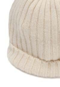 Romige geribbelde gebreide beanie met een zachte textuur en een omgevouwen zoom. Het oppervlak heeft verticale lijnen en een strakke, afgeronde vorm.