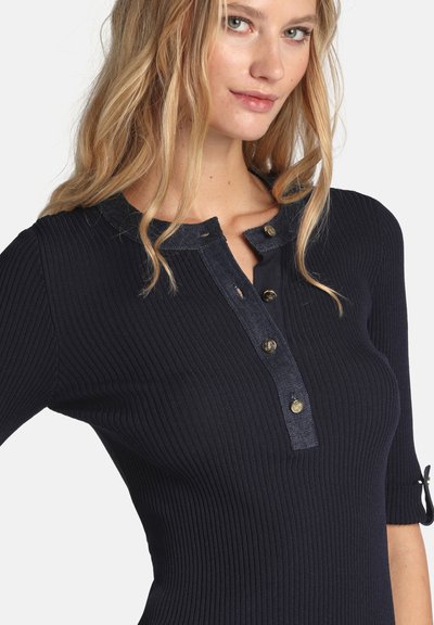 Marineblaues geripptes Strickoberteil mit kurzen Ärmeln, ausgestattet mit einem Denim-Kragen und Knopfdetails, die eine strukturierte und kontrastreiche Designkomponente hinzufügen.