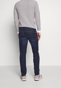 Vaqueros de denim azul oscuro con corte recto, que cuentan con dos bolsillos traseros y detalles de costura sutiles. Combinados con un suéter de punto gris claro.