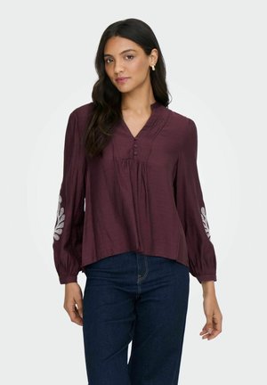 Burgundy, lätt blus med V-ringning, knappslå och dekorativ vit broderi på ärmarna. Lätt kortad design.