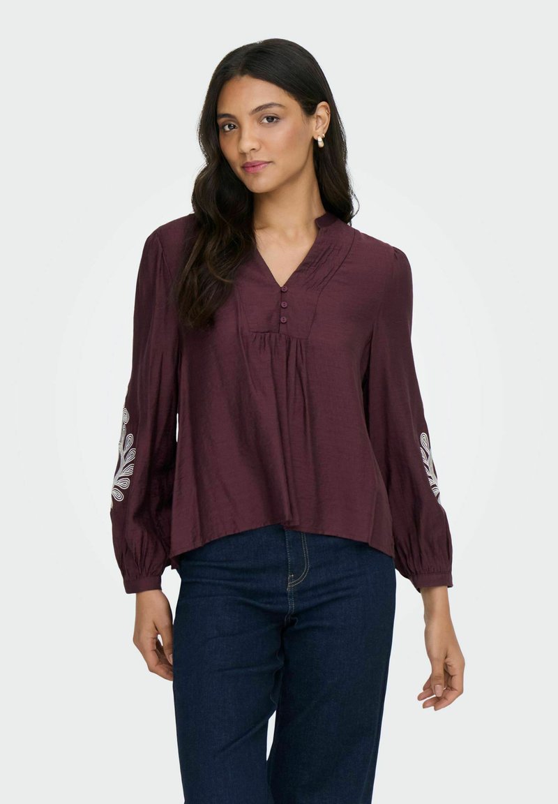 Bordeaux, let blouse i let materiale med V-hals, knaplukning og dekorativt hvidt broderi på ærmerne. Let forkortet design.
