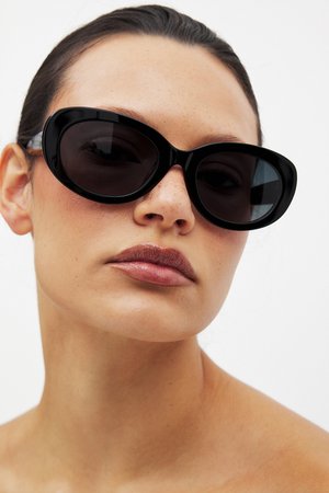 Črne prevelike mačje očala s temnimi lečami; sijoči plastični okvirji; značilna ukrivljena oblika; prozorni detajli na ušesnih delih.