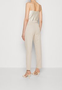 Beige, hoge taille, op maat gemaakte broeken met een gladde textuur en twee achterzakken, gecombineerd met een satijnen, lichtgekleurde top met spaghettibandjes.