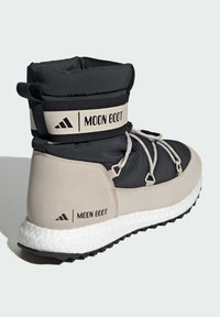 Černé a béžové Moon Boots s nadýchaným svrškem, které mají silnou bílou podrážku, černou gumovou trakci a šedé tkaničky se strapcem s logem.