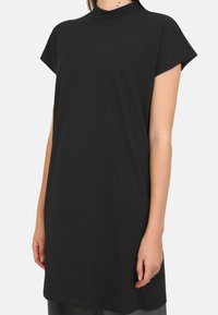 Abito nero a maniche corte con collo alto, realizzato in tessuto morbido. Il design è ampio con una linea dritta e dettagli minimal.