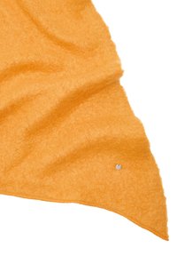 Pomarańczowa tkanina o teksturze, sprawiająca wrażenie miękkości, z zaokrąglonym trójkątnym kształtem i małym metalowym detalem z logo w jednym rogu.