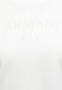 Tissu blanc avec le logo « ARMANI A|X » formé de petits points en relief sur la zone de la poitrine.