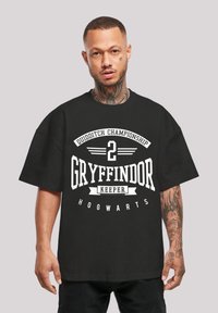 Must mängu shirt, kus on suur suurus ja must värv, millel on valge tekst "Quidditch Championship 2 Gryffindor Keeper Hogwarts" julge, graafilise disainiga.