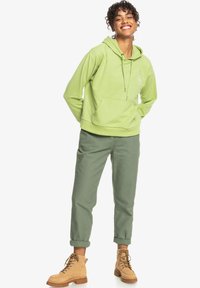 Felpa verde chiaro con tasca a marsupio e cordino. Abbinata a pantaloni verdi con risvolto e stivali beige con lacci.