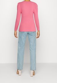 Dopasowany różowy prążkowany top z długim rękawem i marszczonymi ramionami, zestawiony z jasnoniebieskimi jeansami o prostych nogawkach oraz beżowymi sandałami na słupku.