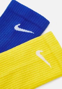 Skarpety Nike w kolorze niebieskim i żółtym, z ryflowaną teksturą i kontrastowymi białymi logo Swoosh na każdej. Każda skarpeta ma inny, żywy kolor.